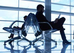 Two business partners reading at the airport on background of their colleague standing by the window